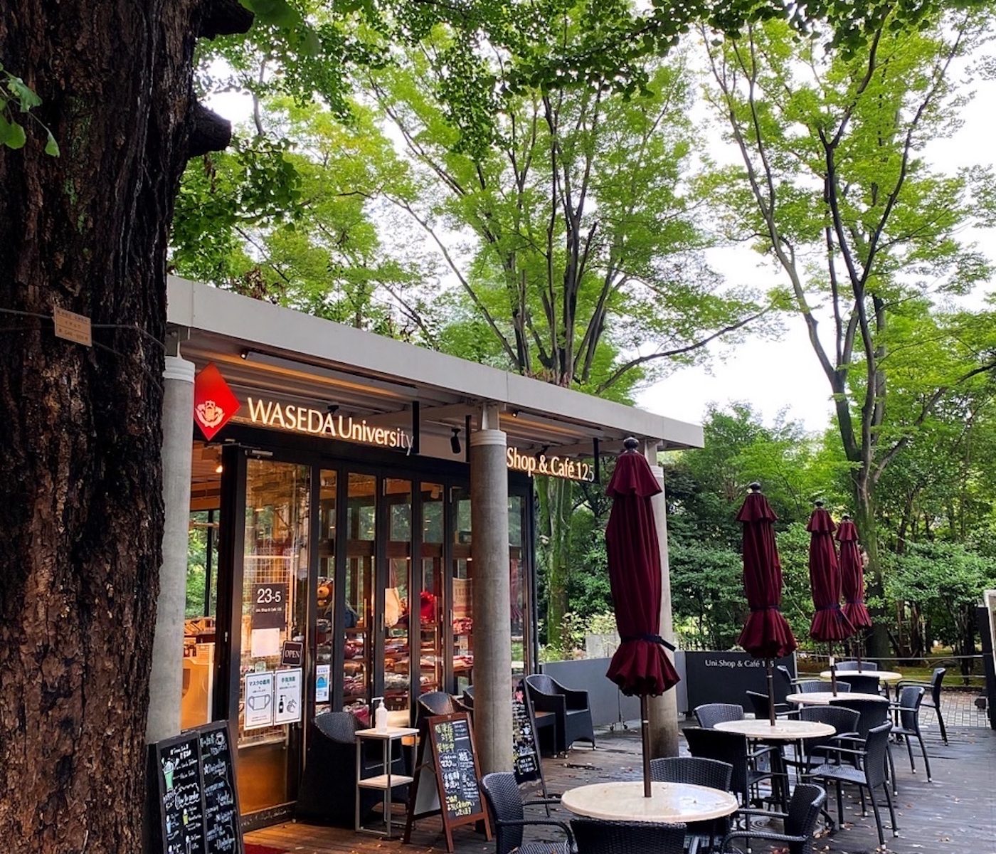 Photo of the Waseda University Uni Shop & Cafe 125. Outdoor seating in the front, trees in the background.